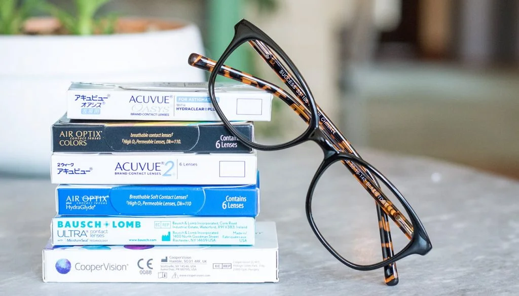 a stack of contact lens boxes with glasses perched next to them