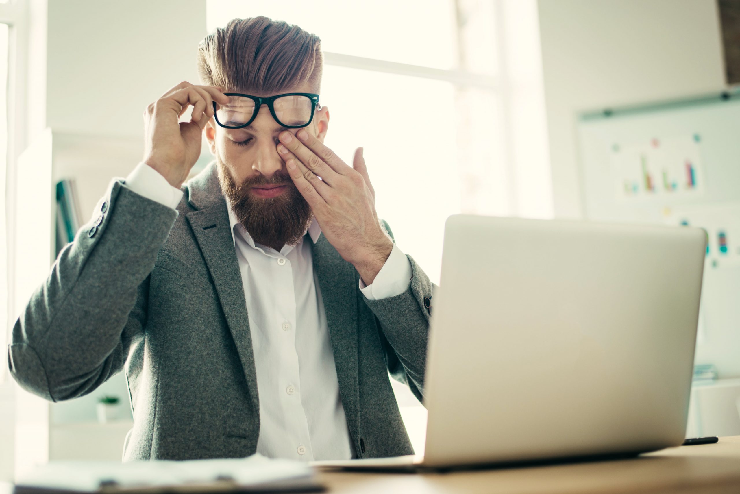 Young tired businessmsn is touching his eye, taking off the glasses, he is experiencing digital eye strain