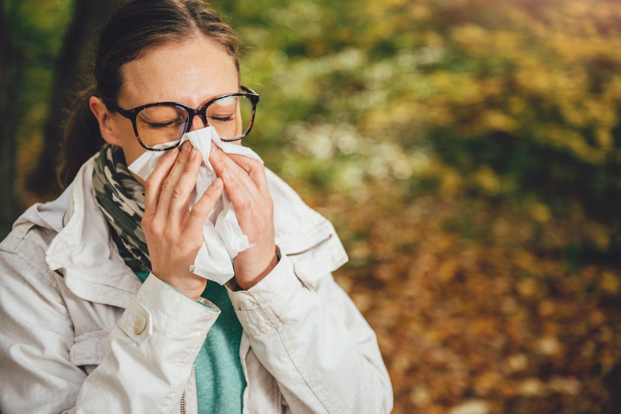 Woman with glasses blowing her nose in the park