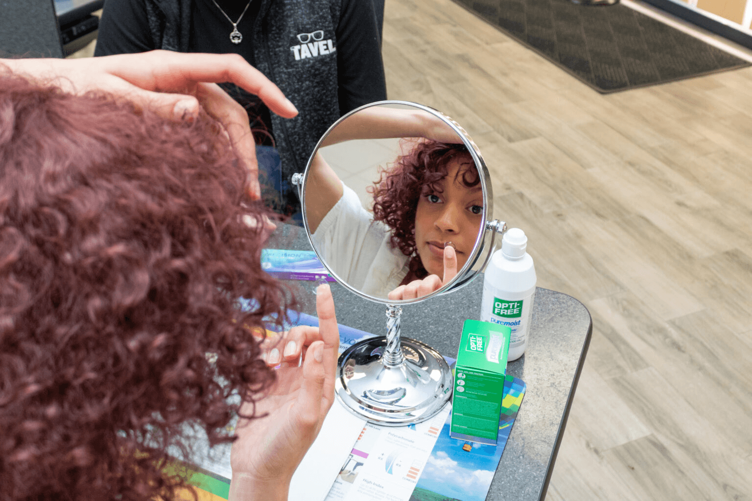 Lady putting in contacts at Dr. Tavel while looking in mirror.