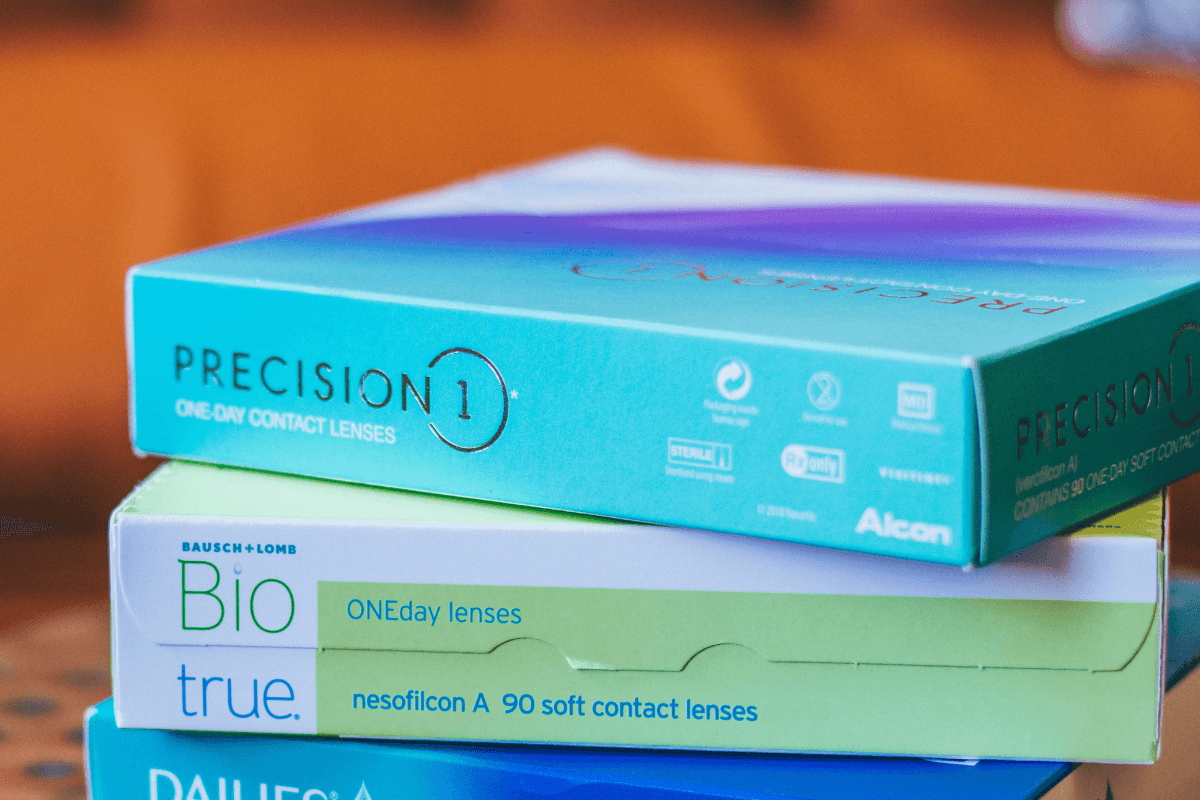 stack of daily disposable contact lens boxes with brands like Precision 1 and Biotrue